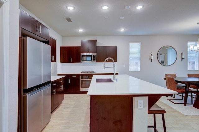 kitchen featuring light hardwood / wood-style flooring, sink, appliances with stainless steel finishes, and an island with sink