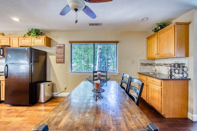 kitchen featuring a textured ceiling, ceiling fan, black appliances, hardwood / wood-style flooring, and dark stone countertops