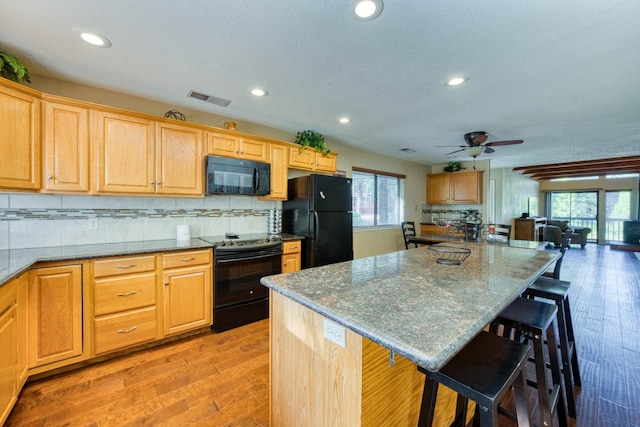 kitchen featuring a breakfast bar, light hardwood / wood-style floors, a healthy amount of sunlight, and black appliances