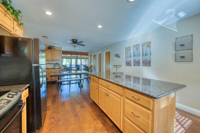 kitchen featuring ceiling fan, black appliances, dark stone countertops, dark hardwood / wood-style floors, and a kitchen island