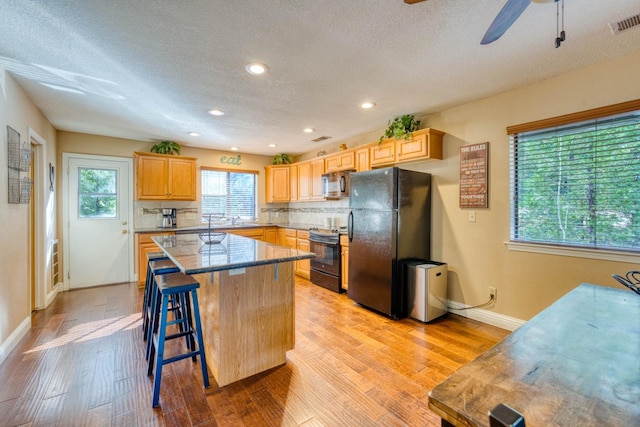 kitchen with a center island, light hardwood / wood-style flooring, backsplash, a breakfast bar area, and appliances with stainless steel finishes