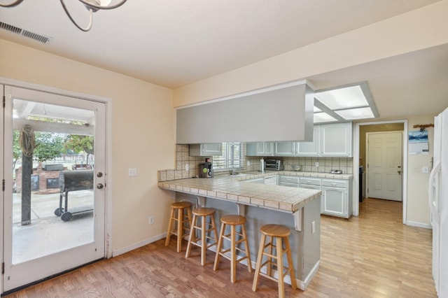 kitchen featuring kitchen peninsula, white cabinets, decorative backsplash, and a breakfast bar area