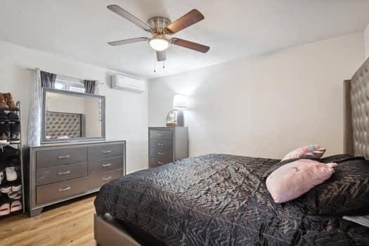 bedroom featuring ceiling fan, a wall unit AC, and light hardwood / wood-style flooring