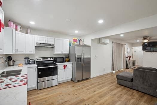 kitchen featuring sink, light hardwood / wood-style flooring, stainless steel appliances, a wall mounted AC, and white cabinets