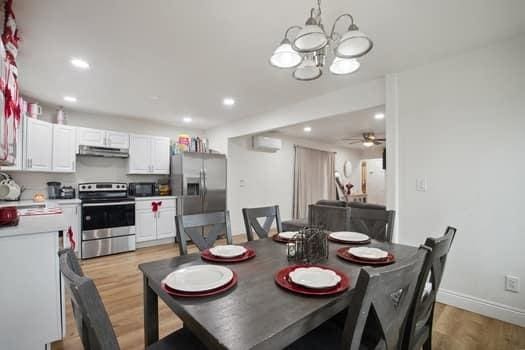 dining space featuring ceiling fan with notable chandelier, a wall unit AC, and light wood-type flooring