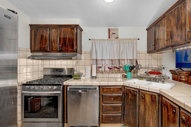 kitchen featuring tile countertops, decorative backsplash, stainless steel appliances, and sink