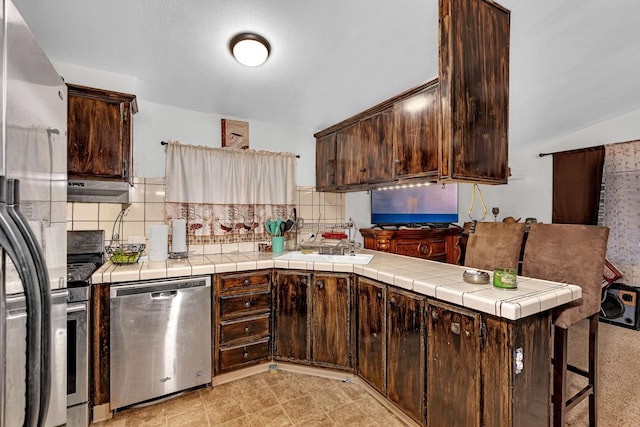 kitchen with kitchen peninsula, tile counters, dark brown cabinets, and appliances with stainless steel finishes