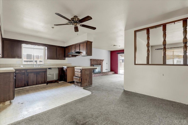 kitchen with kitchen peninsula, a brick fireplace, ceiling fan, light colored carpet, and dark brown cabinetry