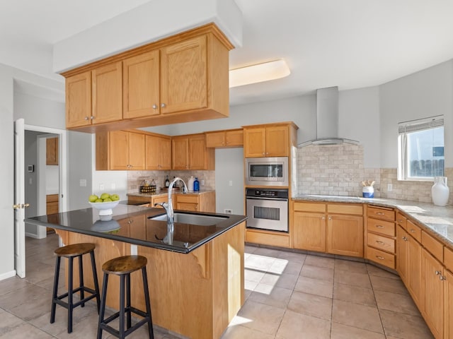 kitchen with light tile patterned flooring, sink, appliances with stainless steel finishes, a kitchen island with sink, and wall chimney range hood