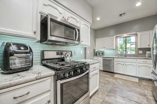 kitchen featuring white cabinets, appliances with stainless steel finishes, decorative backsplash, and sink