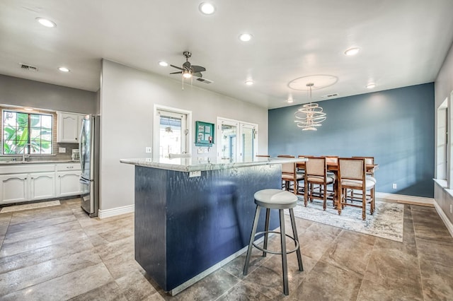 kitchen featuring pendant lighting, white cabinets, ceiling fan, a breakfast bar area, and stainless steel refrigerator