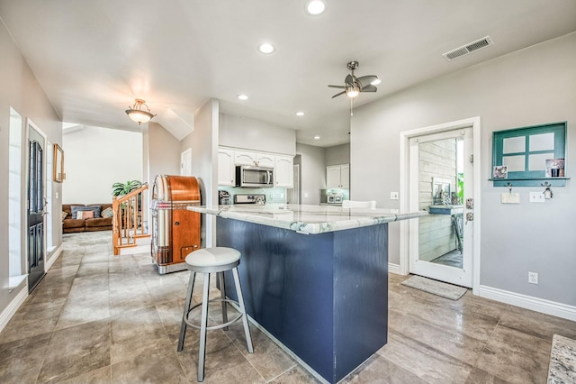 kitchen with ceiling fan, light stone countertops, a kitchen breakfast bar, white cabinets, and appliances with stainless steel finishes