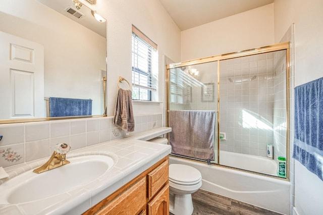 full bathroom featuring vanity, shower / bath combination with glass door, hardwood / wood-style flooring, toilet, and tasteful backsplash