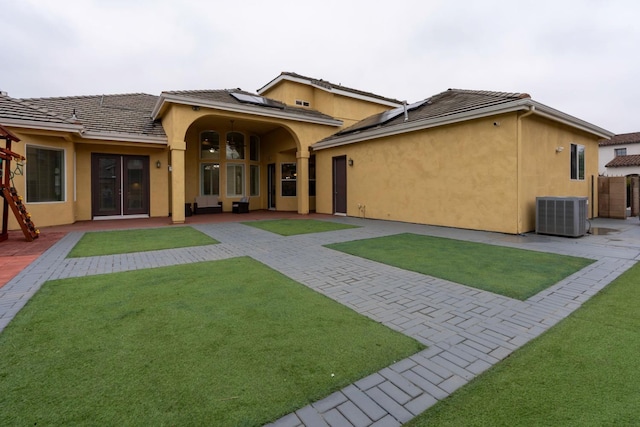 back of property with solar panels, a yard, a patio, and central AC