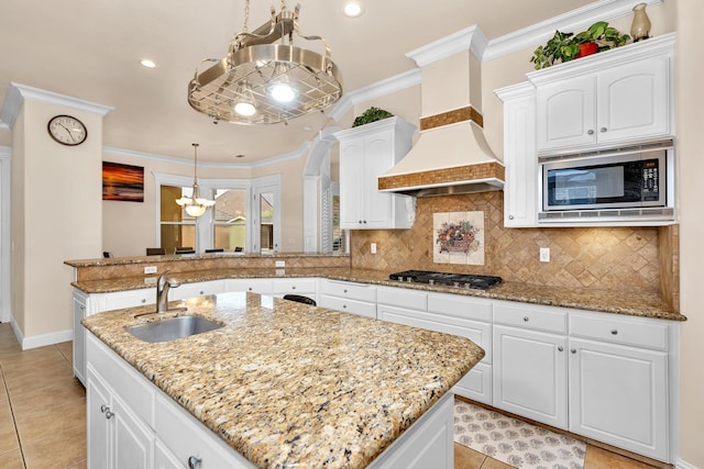 kitchen with ornamental molding, custom range hood, stainless steel appliances, sink, and decorative light fixtures