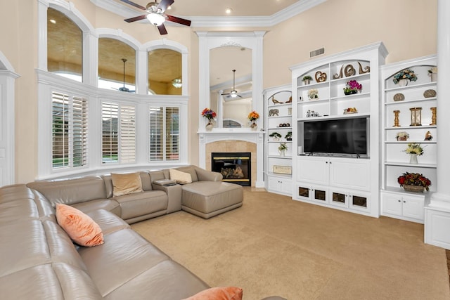 living room with a tiled fireplace, crown molding, a towering ceiling, and light colored carpet