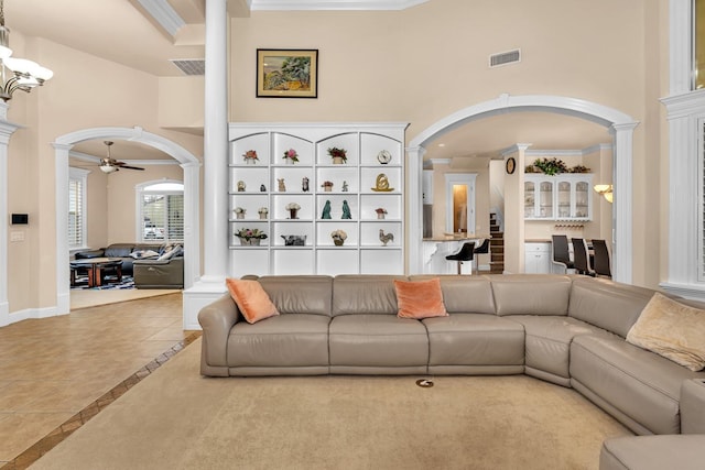 living room featuring a towering ceiling, ornate columns, ceiling fan, crown molding, and light tile patterned floors