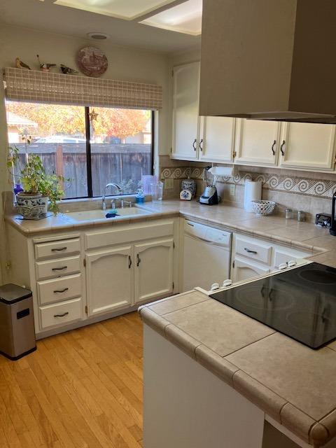 kitchen featuring tile countertops, white cabinetry, white dishwasher, and light wood-type flooring