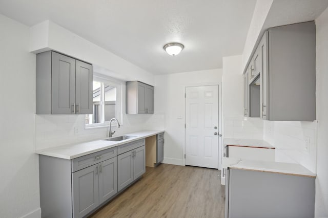 kitchen with backsplash, gray cabinetry, sink, and light hardwood / wood-style floors