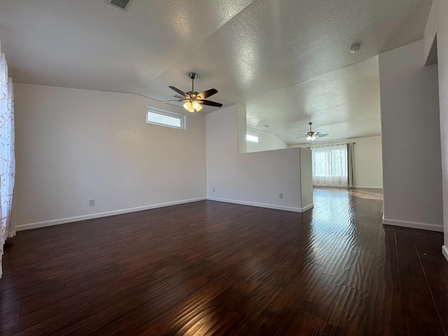 unfurnished room featuring dark hardwood / wood-style floors, a healthy amount of sunlight, a textured ceiling, and vaulted ceiling