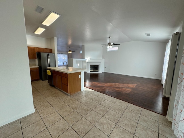 kitchen featuring a kitchen island with sink, vaulted ceiling, ceiling fan, stainless steel fridge, and light wood-type flooring