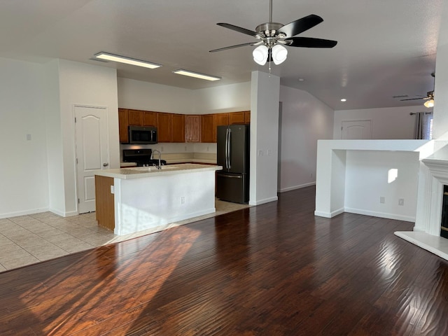 kitchen with ceiling fan, light hardwood / wood-style flooring, an island with sink, vaulted ceiling, and appliances with stainless steel finishes