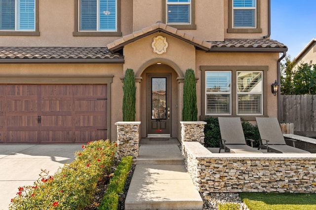 property entrance with driveway, a garage, a tile roof, fence, and stucco siding