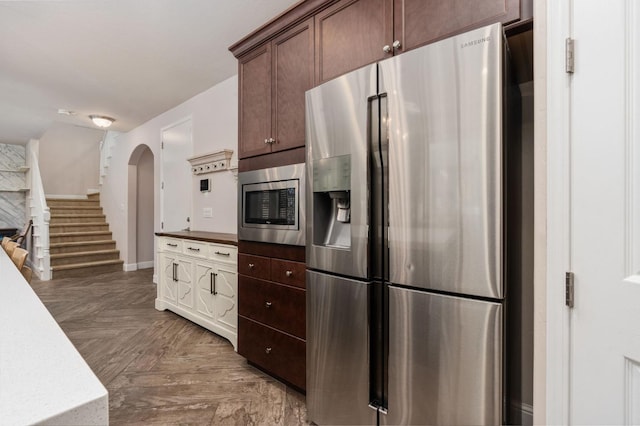 kitchen with stainless steel appliances, arched walkways, dark brown cabinets, and baseboards