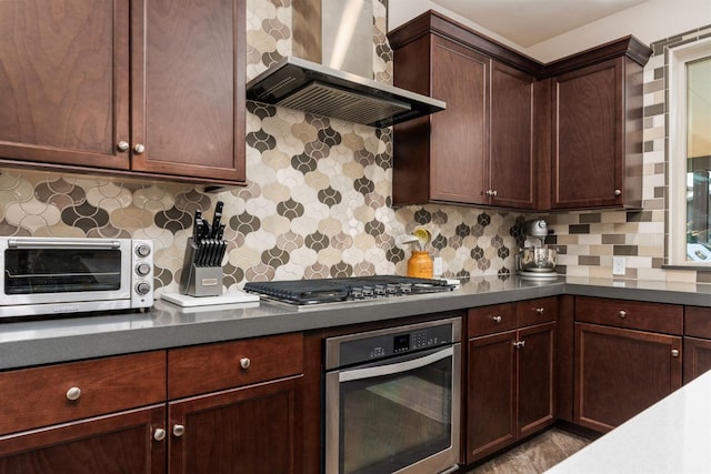 kitchen with a toaster, dark countertops, decorative backsplash, appliances with stainless steel finishes, and wall chimney range hood