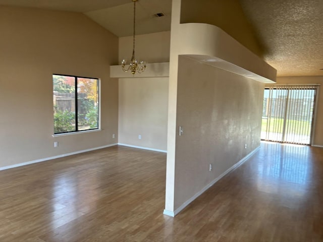 unfurnished room featuring a textured ceiling, hardwood / wood-style floors, a chandelier, and lofted ceiling