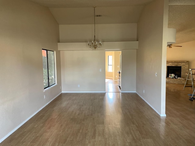 spare room featuring high vaulted ceiling, dark hardwood / wood-style floors, a fireplace, and a wealth of natural light