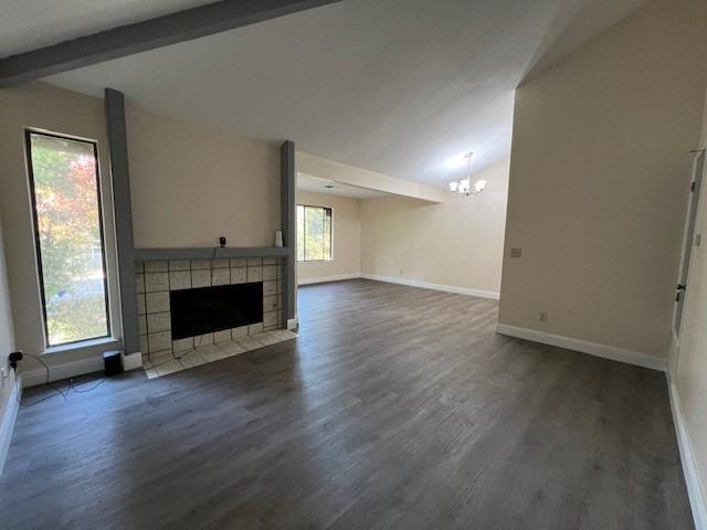 unfurnished living room featuring a tiled fireplace, dark hardwood / wood-style flooring, a notable chandelier, and vaulted ceiling with beams