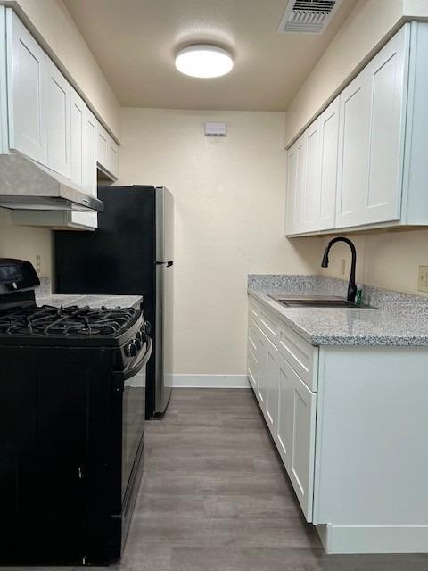 kitchen featuring light stone countertops, gas stove, sink, white cabinets, and light hardwood / wood-style floors