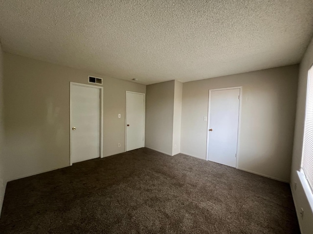 empty room with dark carpet and a textured ceiling