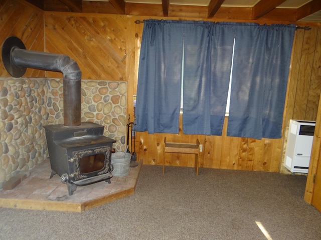 carpeted living room with beam ceiling, a wood stove, wood walls, and radiator