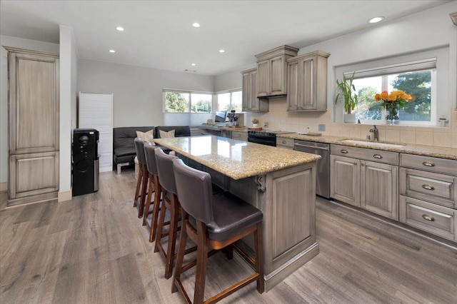 4481 N Palm, Fresno, CA 93704 - kitchen featuring stainless steel dishwasher, a breakfast bar area, wood finished floors, decorative backsplash, and a kitchen island