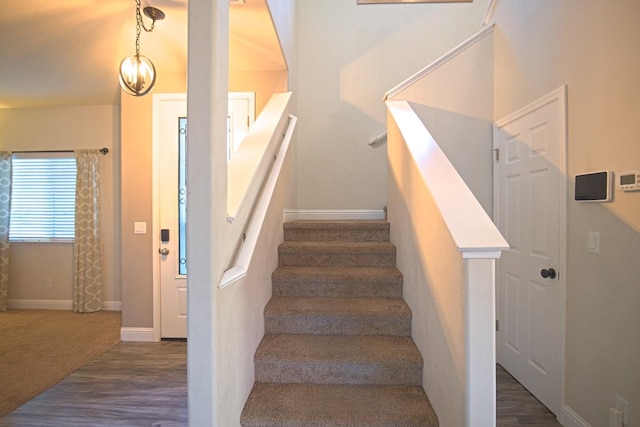 staircase with wood-type flooring and an inviting chandelier