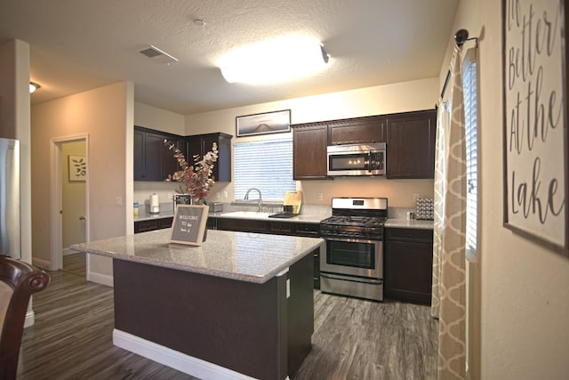 kitchen with dark brown cabinets, dark hardwood / wood-style flooring, stainless steel appliances, and a kitchen island