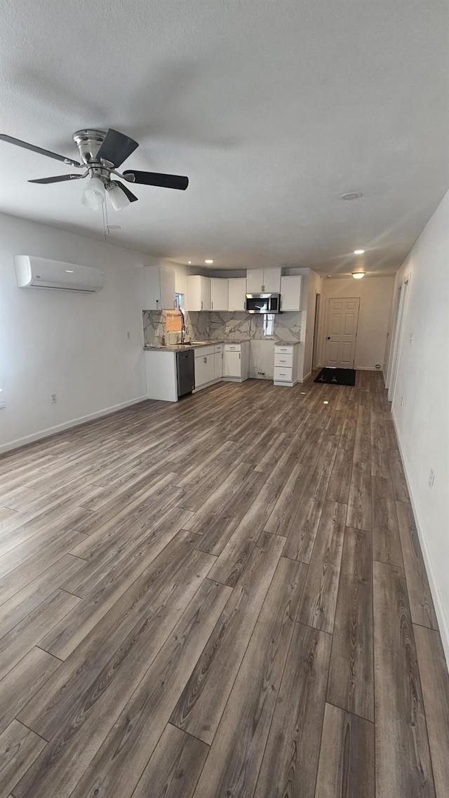 unfurnished living room with dark wood-type flooring, an AC wall unit, sink, ceiling fan, and a textured ceiling