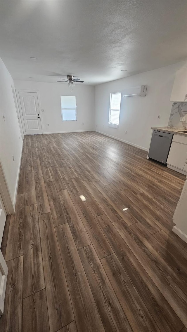 unfurnished living room with a textured ceiling, dark hardwood / wood-style floors, a wall unit AC, and ceiling fan