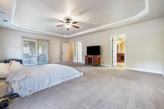 carpeted bedroom with ceiling fan, a tray ceiling, ensuite bathroom, and ornamental molding