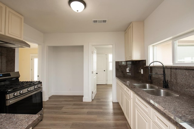 kitchen featuring decorative backsplash, dark hardwood / wood-style flooring, dark stone counters, sink, and stainless steel range with gas cooktop