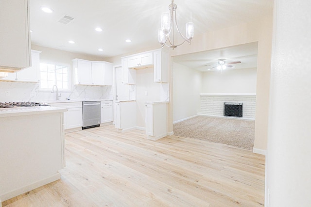 kitchen featuring stainless steel dishwasher, a fireplace, pendant lighting, white cabinets, and light hardwood / wood-style floors