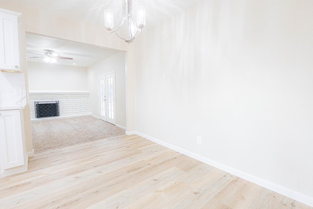 unfurnished living room with ceiling fan with notable chandelier, light hardwood / wood-style floors, a fireplace, and french doors