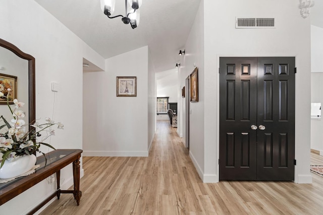 hallway with an inviting chandelier, lofted ceiling, and light wood-type flooring