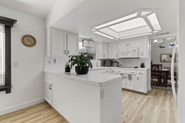 kitchen with kitchen peninsula, light wood-type flooring, tasteful backsplash, tile countertops, and white cabinets