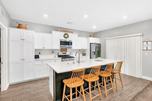 kitchen featuring sink, a center island with sink, a kitchen breakfast bar, stainless steel appliances, and white cabinets