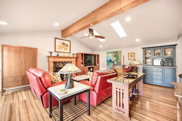 living room with ceiling fan, vaulted ceiling with skylight, a high end fireplace, and light hardwood / wood-style floors