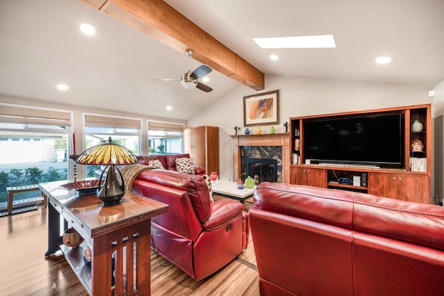 living room with a high end fireplace, light hardwood / wood-style flooring, lofted ceiling with skylight, and ceiling fan