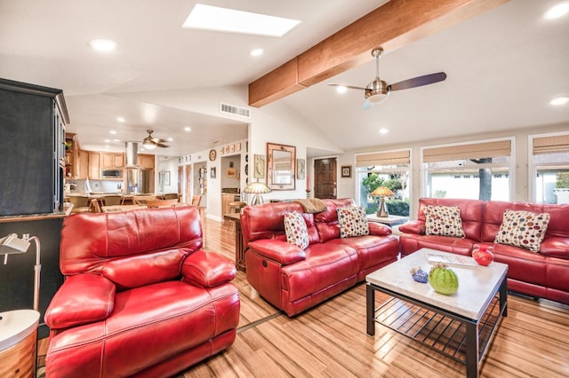 living room featuring ceiling fan, vaulted ceiling with skylight, and light hardwood / wood-style floors